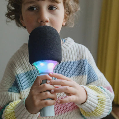 Child holding a microphone with colorful lights, wearing a striped sweater.