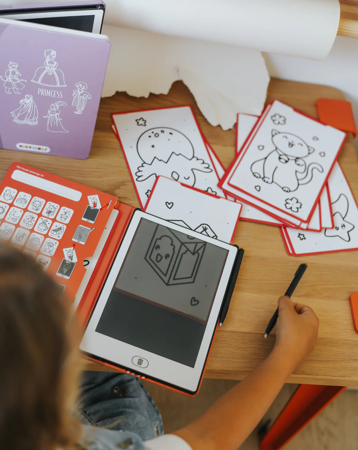 Child using a digital drawing tablet with coloring sheets on a table