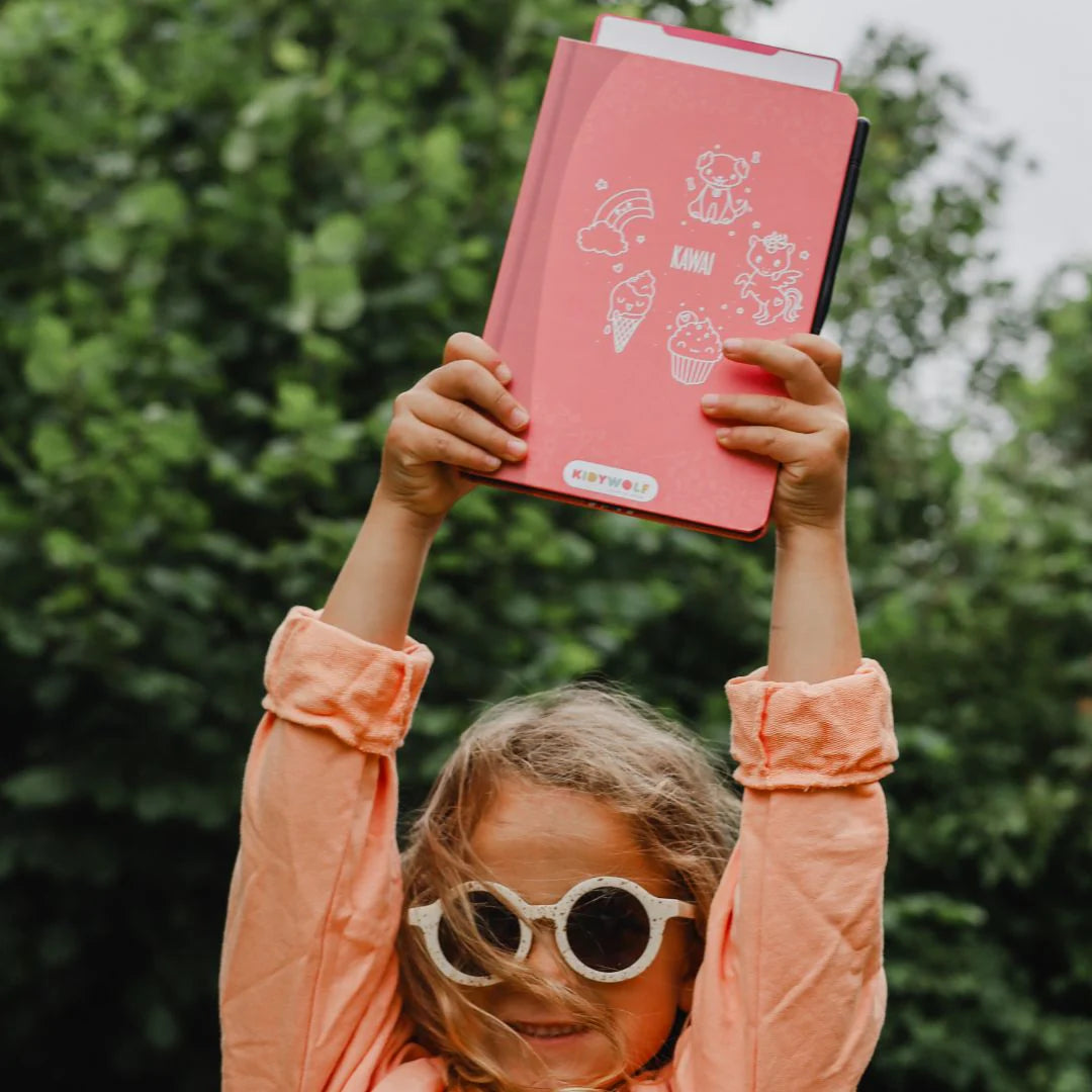 Child holding up a pink book with illustrations outdoors