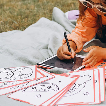 Child coloring on a tablet with coloring sheets outdoors