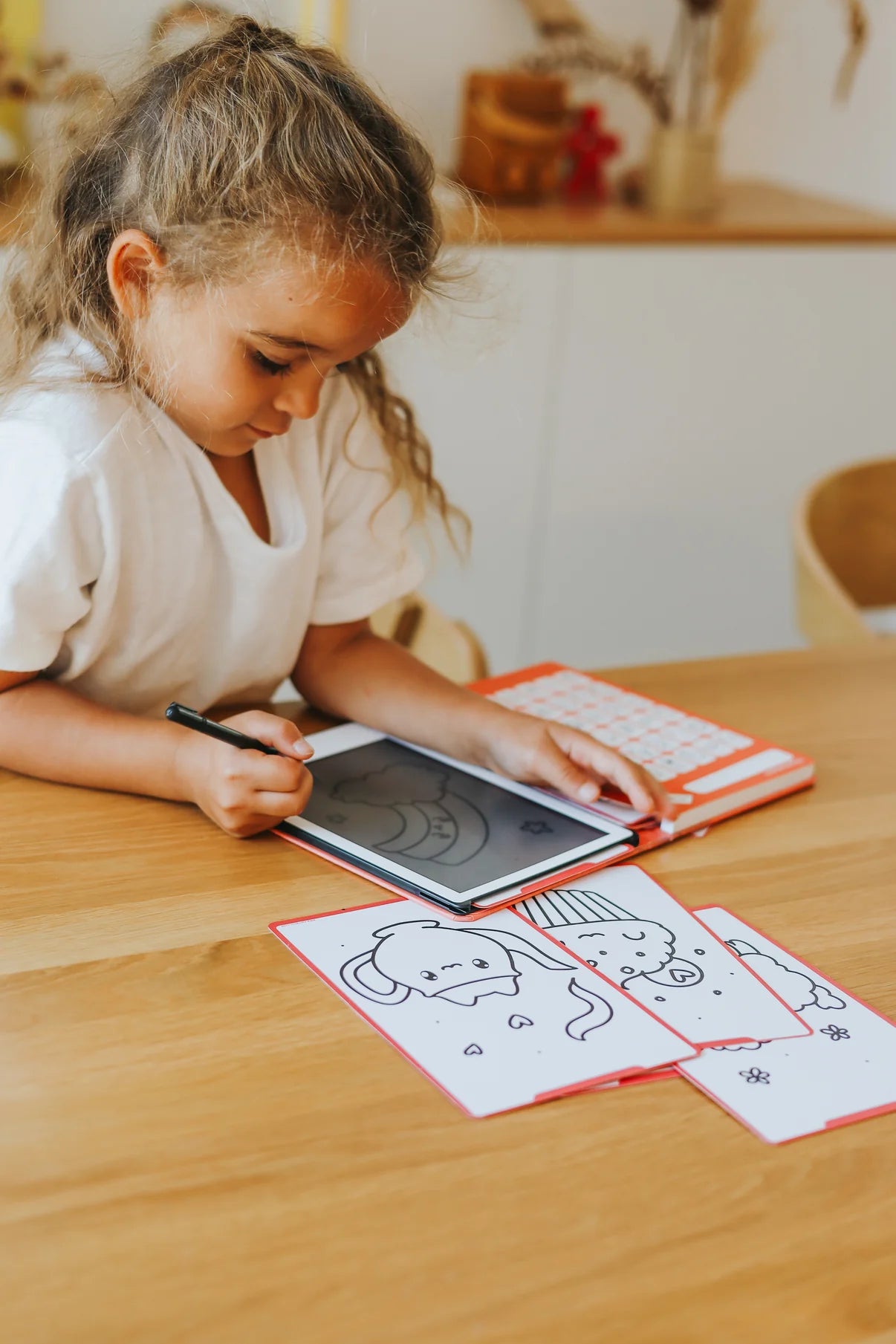 Child using a tablet with coloring books on a wooden table