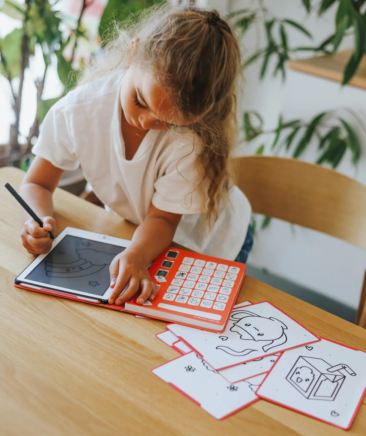 Child using a small tablet with keyboard at a table, surrounded by printed pages.