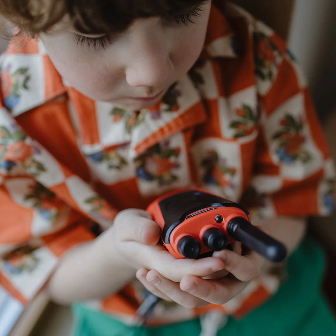 Child holding a red and black toy walkie-talkie, wearing a patterned shirt.