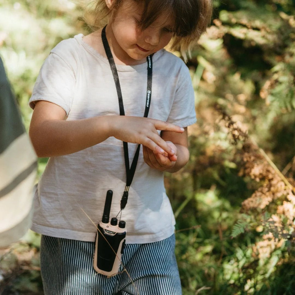 Child outdoors with a walkie-talkie, surrounded by greenery