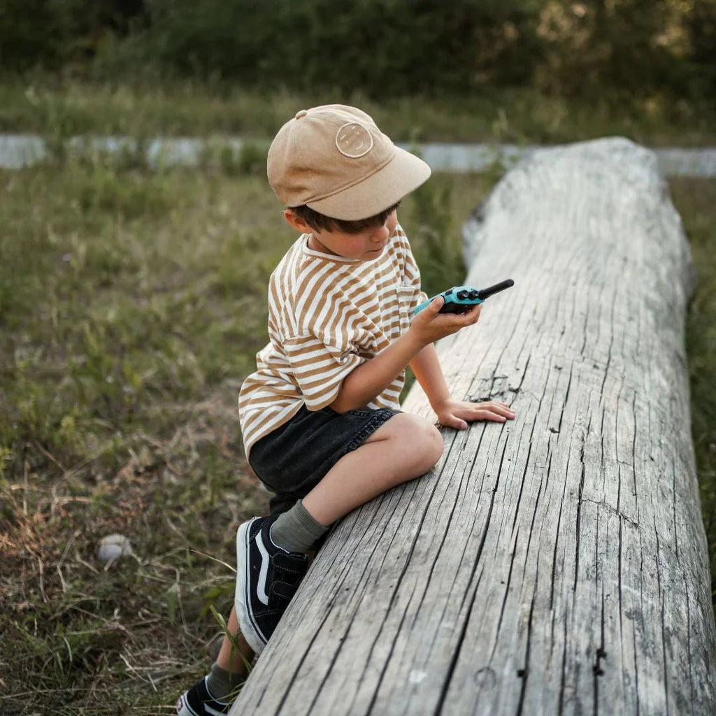 Child sitting on a log outdoors, holding a walkie-talkie