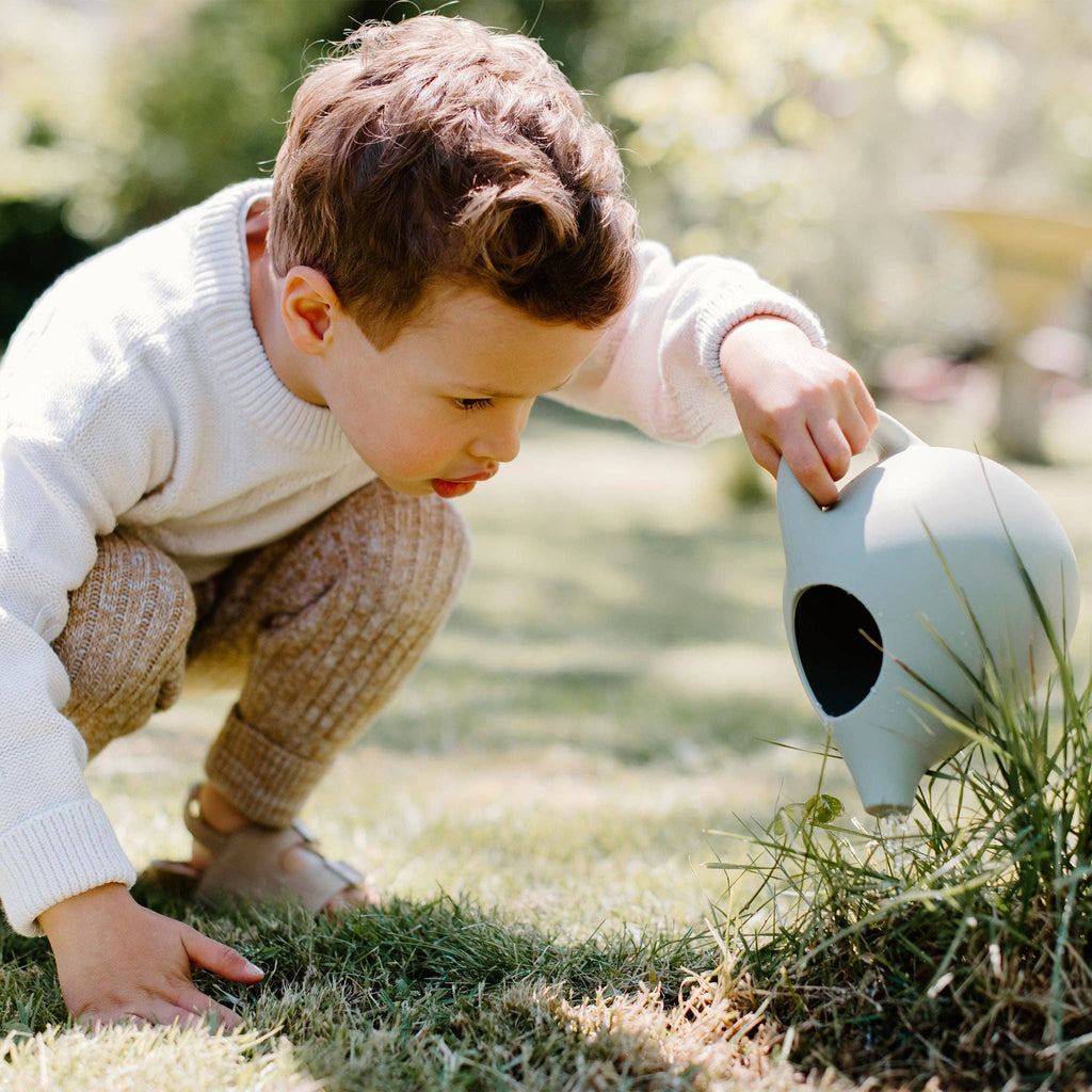 Child with silicone watering can in garden setting.