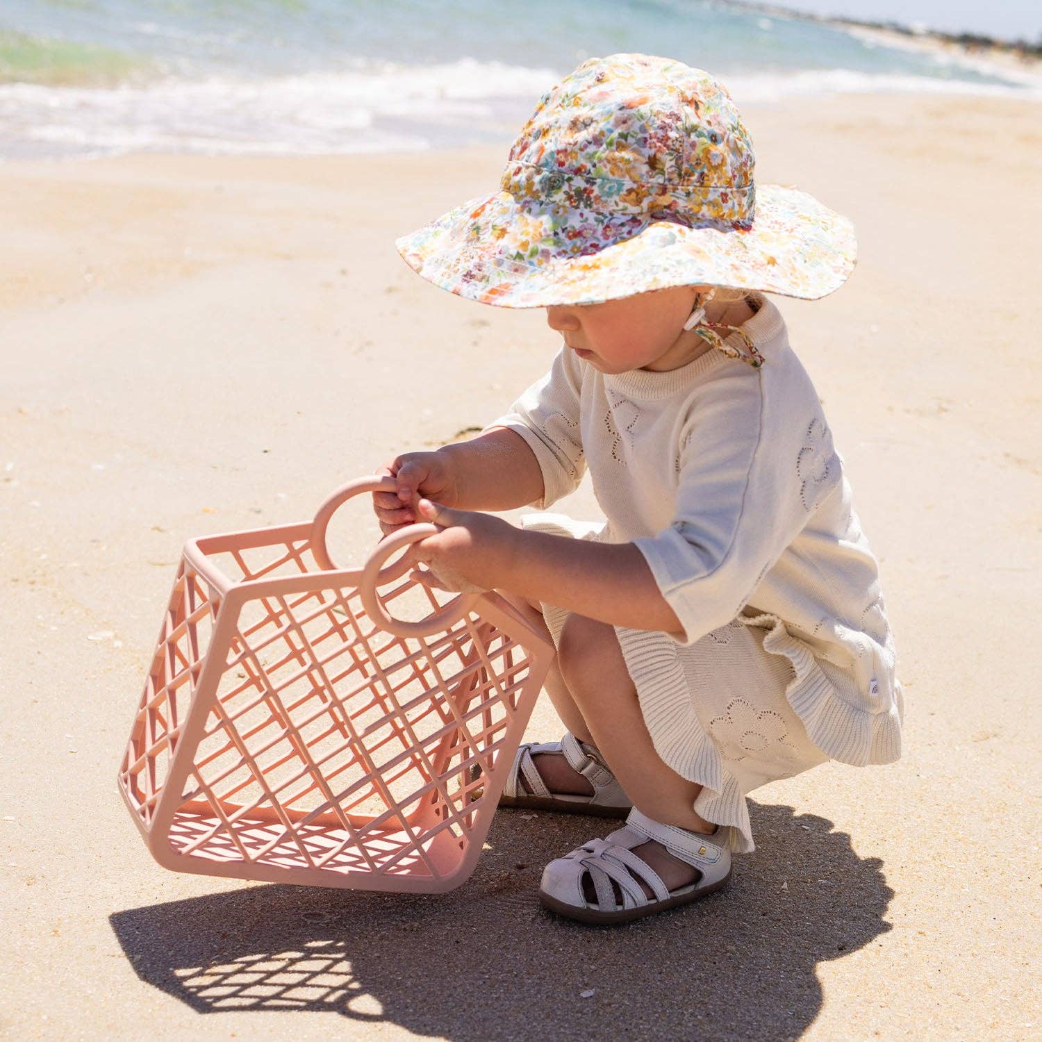 Child at the beach holding pink silicone bag.