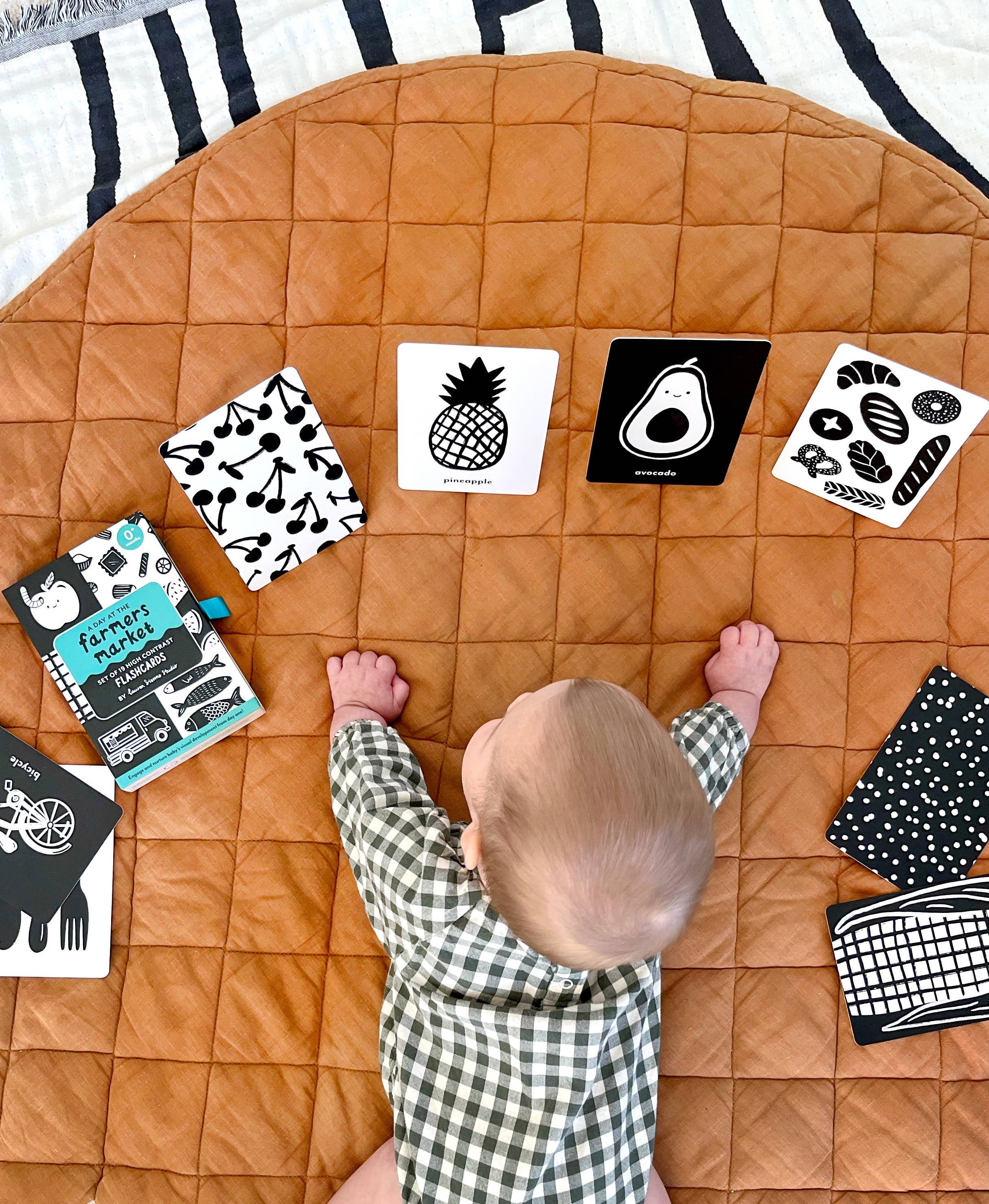 Baby playing with educational cards on a brown quilted play mat.