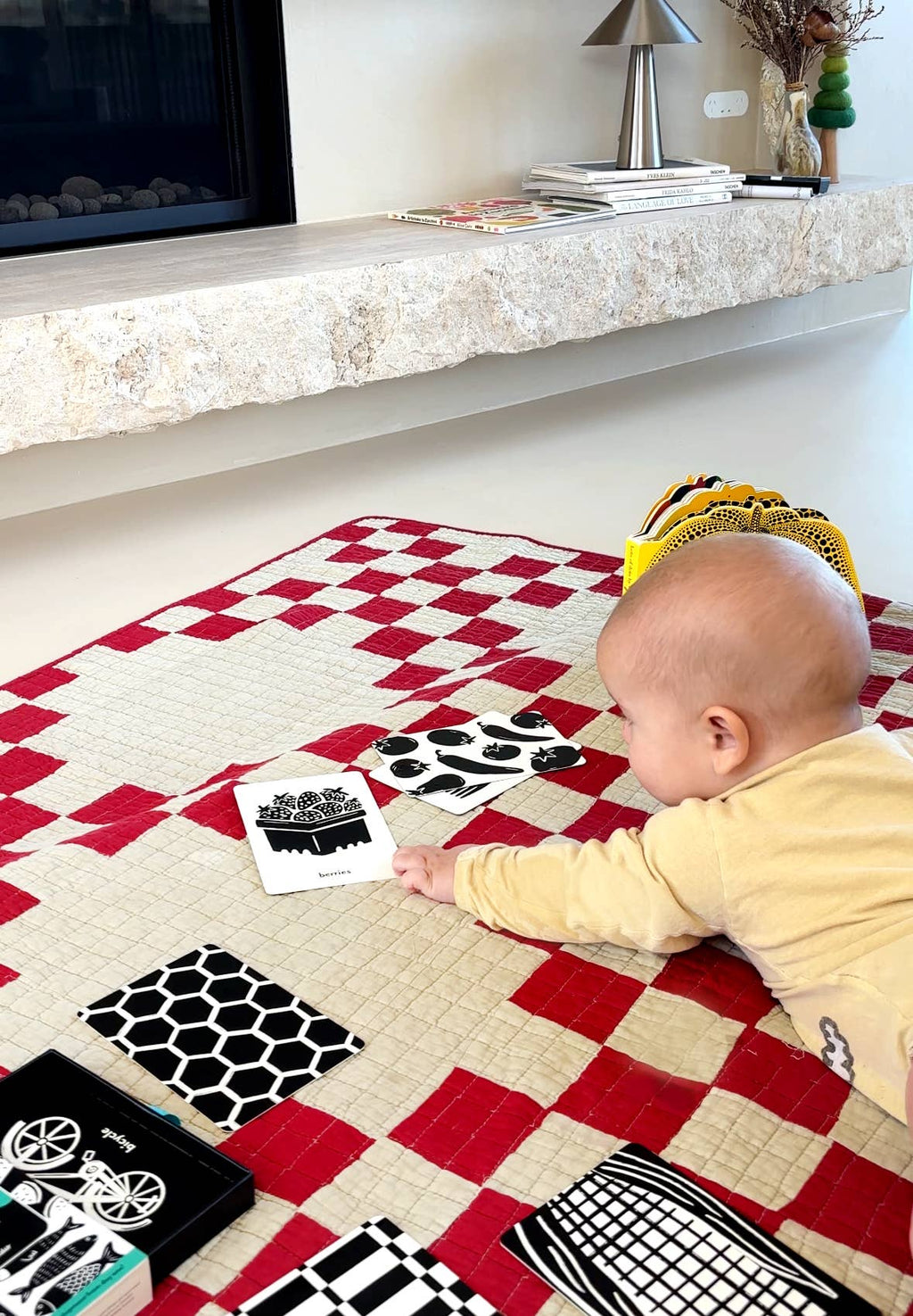 Baby playing with patterned cards on a checkered rug in a living room.