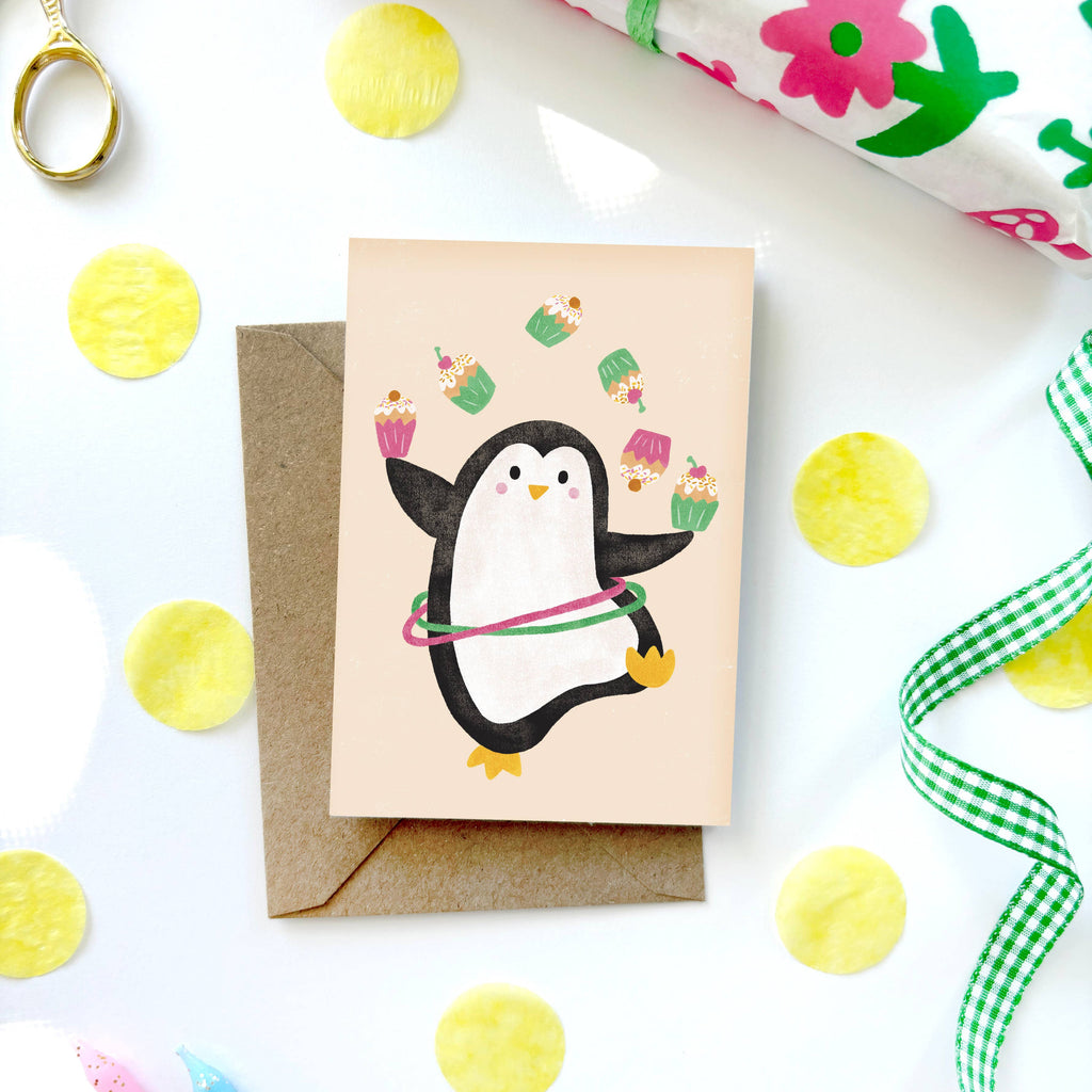 Greeting card with a penguin design on a white surface with decorative items.