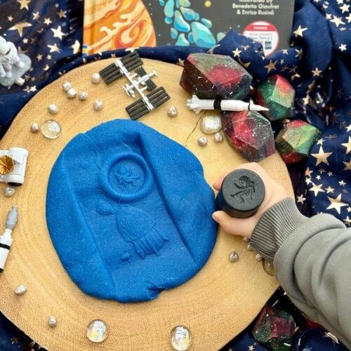 Decorative space-themed tray with blue mold, small rockets, and crystals on a starry background.