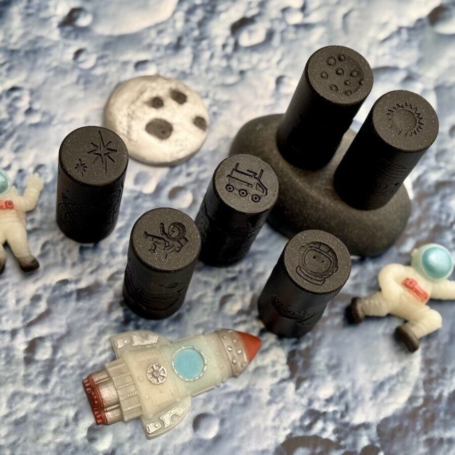 Set of black stamps with designs on a textured surface resembling the moon's surface.