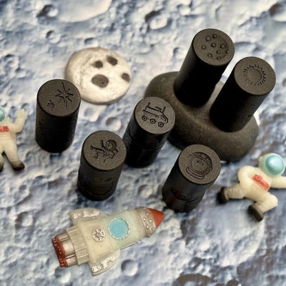 Set of black stamps with designs on a textured surface resembling the moon's surface.