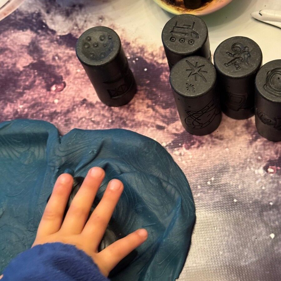 Black cylindrical objects with symbols on a textured surface, one being held by a hand.