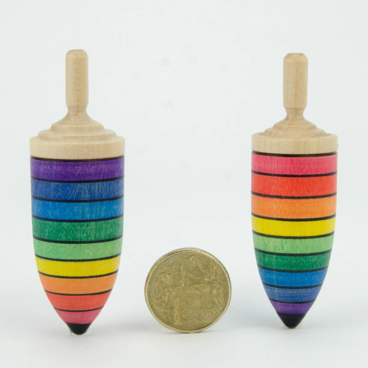 Two rainbow-striped wooden spin tops with a coin for scale on a white background