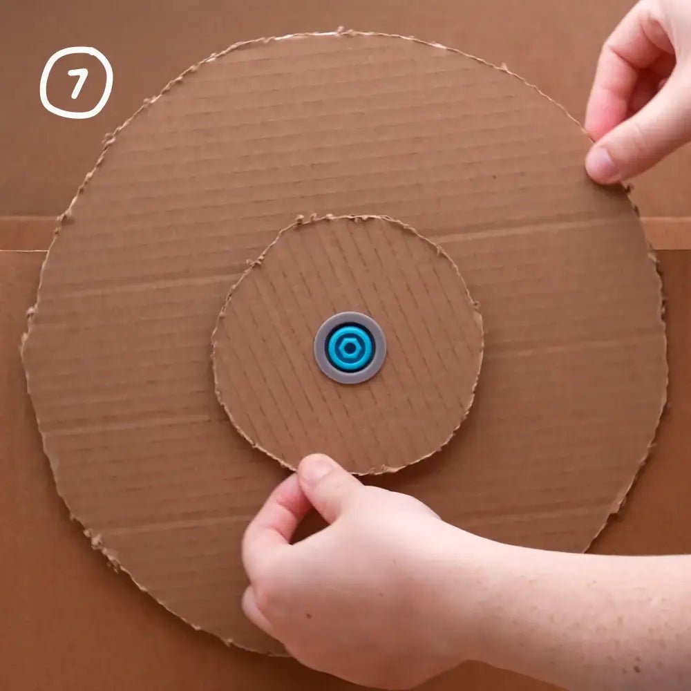 Cardboard circle with a blue and gray center held by hands on a brown background