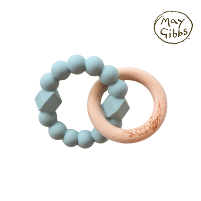 A sage-colored silicone teething ring attached to a beech wood teething ring, both designed by May Gibbs.