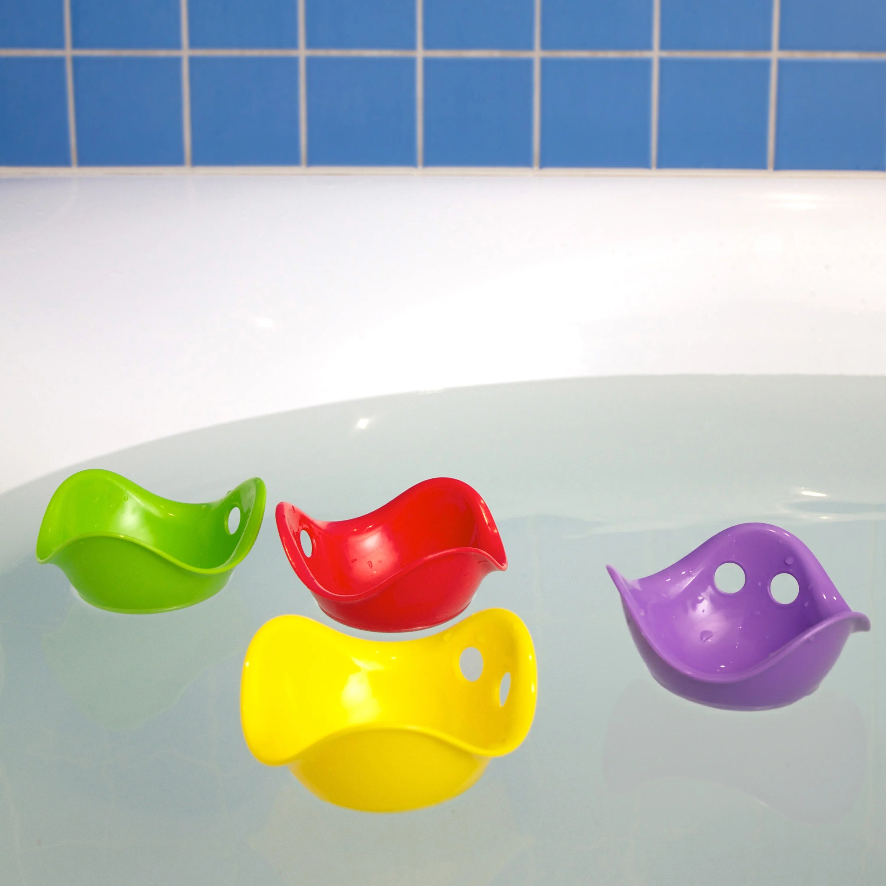 Four colorful bird-shaped cups on a bathtub with a blue tiled wall background.
