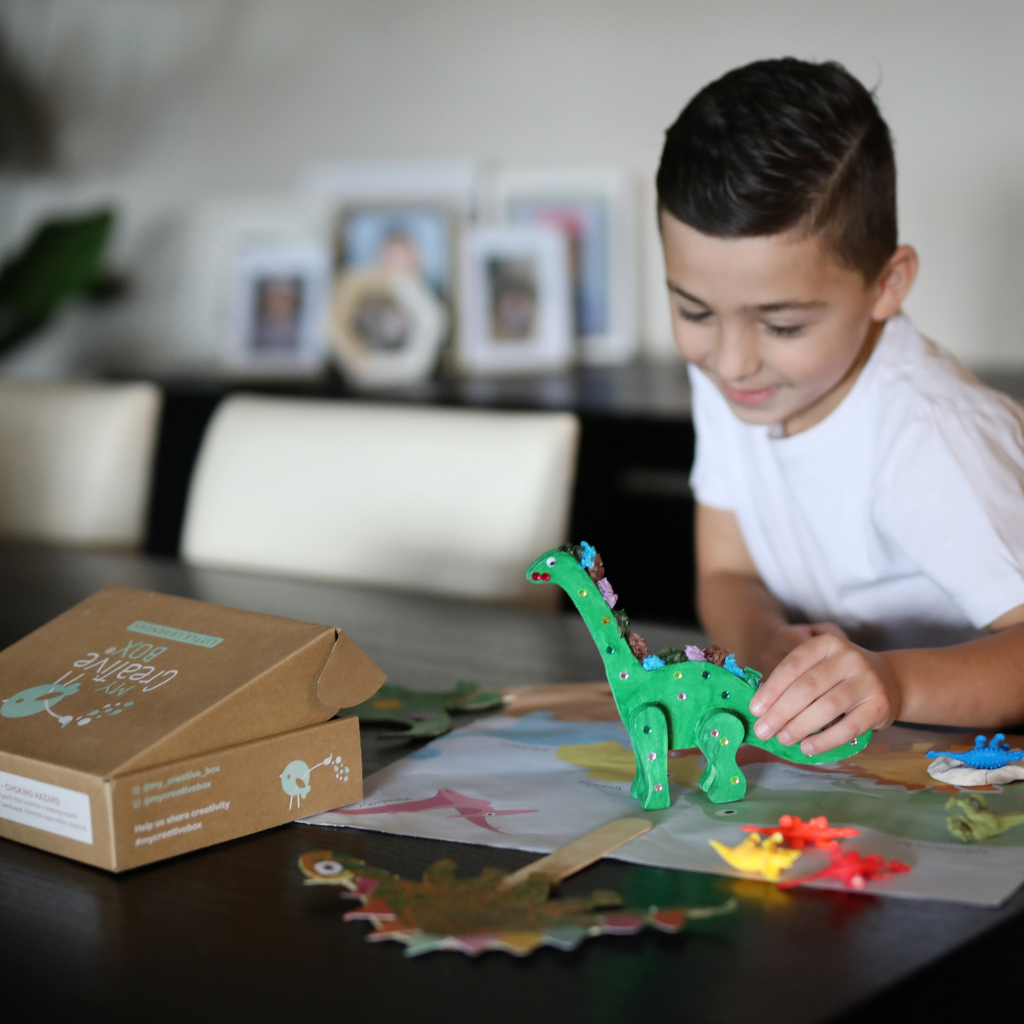 Child holding craft dinosaur in a dining room setting.