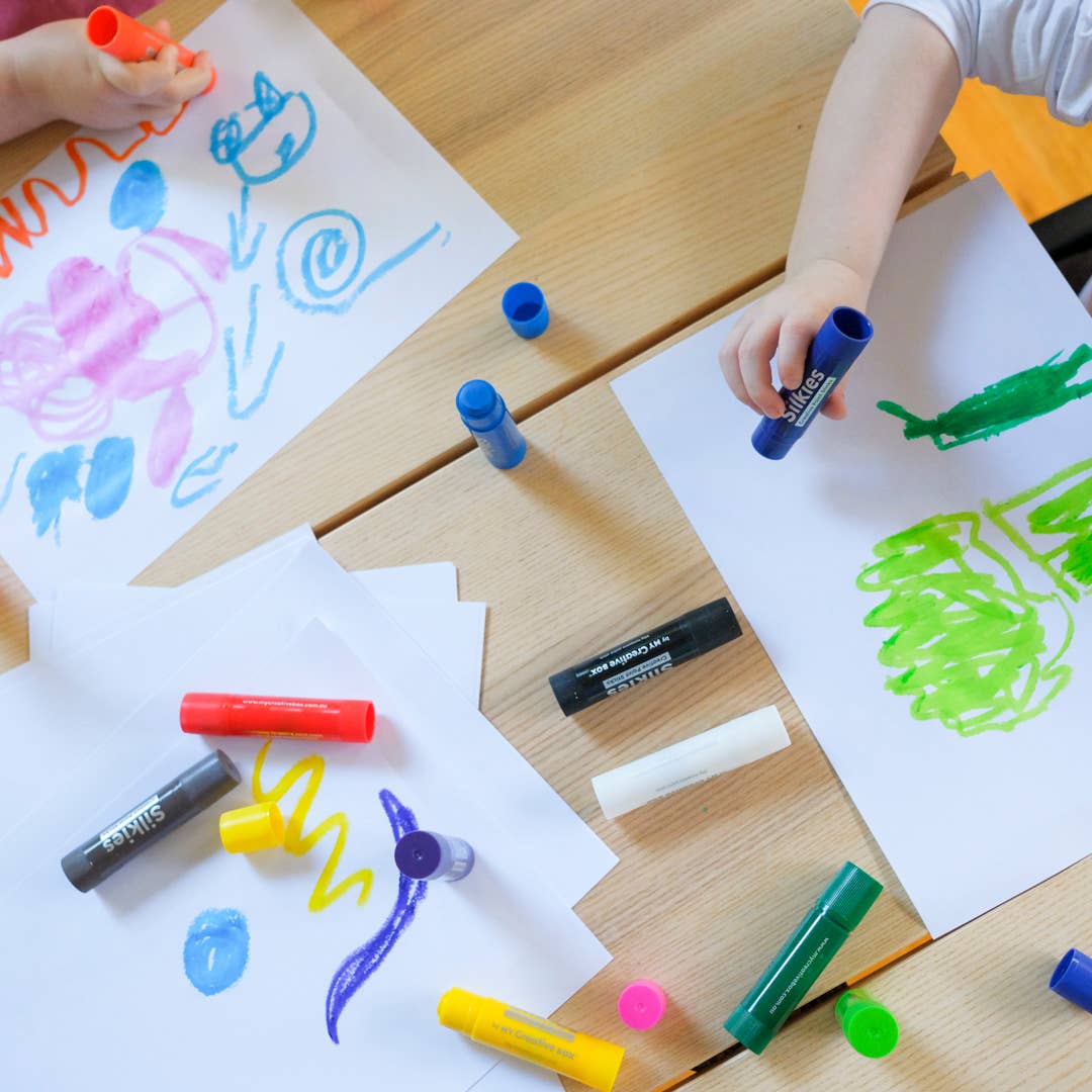 Child holding silkies and drawing on white paper at a table.