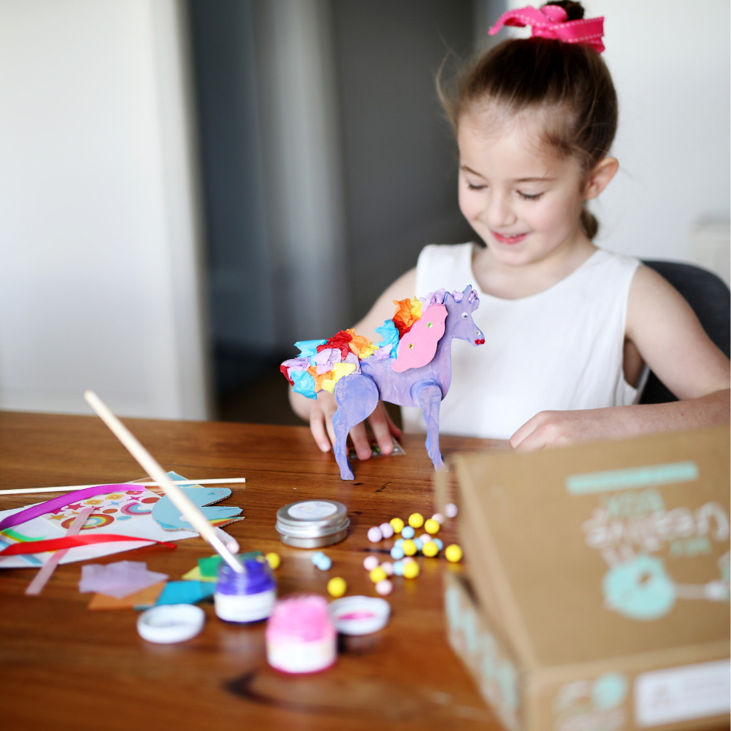 Child with craft unicorn in a dining room setting. 