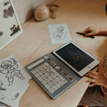 Person using a small electronic device with a keyboard and screen on a wooden table, surrounded by printed cards.