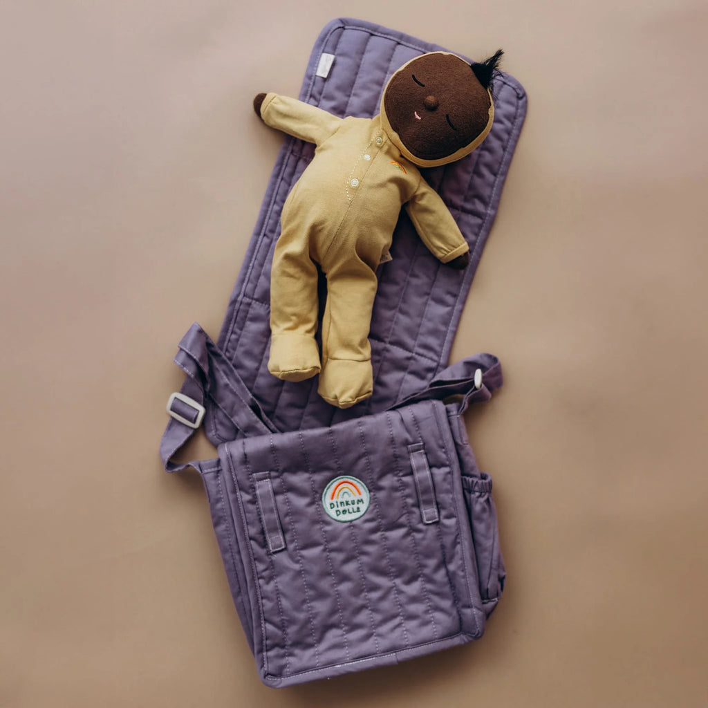 Purple baby carrier with a yellow baby outfit on a beige background