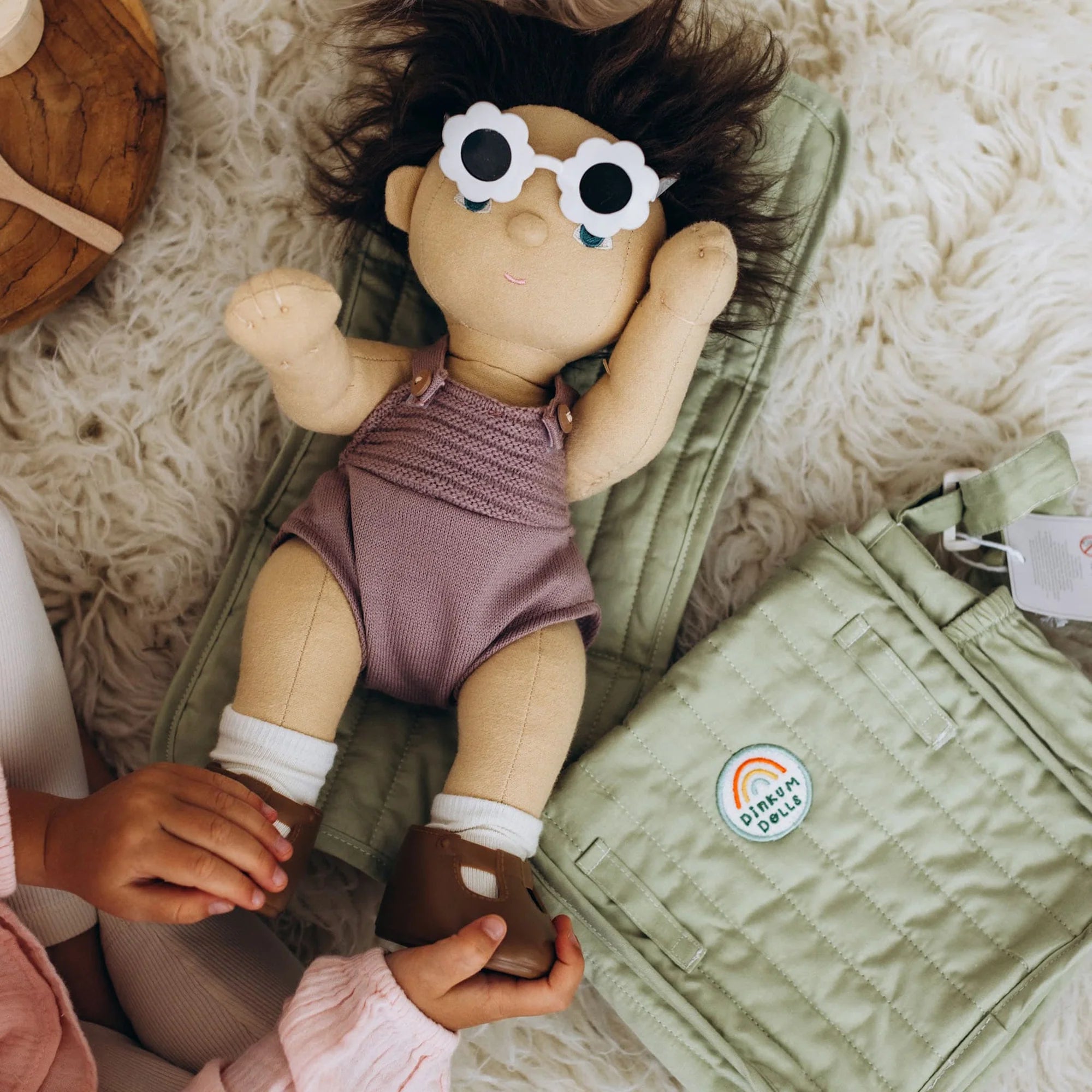 Child holding a plush toy with sunglasses on a soft surface