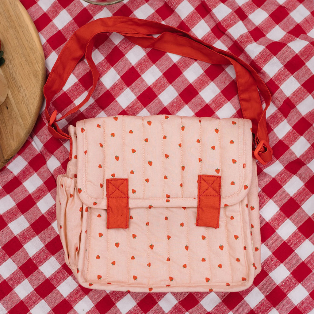 Pink bag with orange polka dots and straps on a red and white checkered tablecloth.