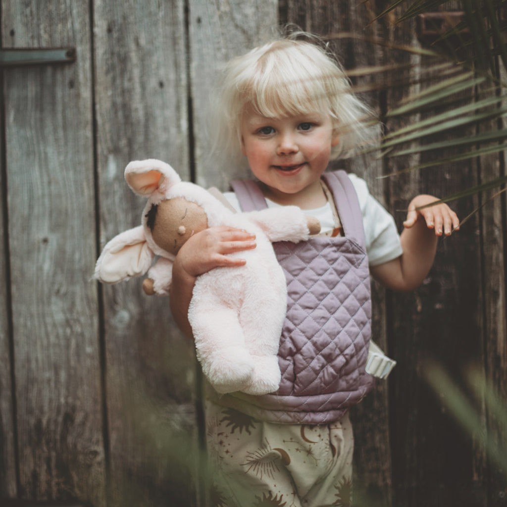 Child holding a plush toy in front of a wooden fence