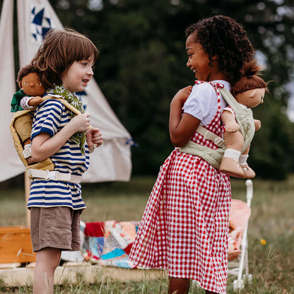 Two children playing with dolls outdoors, with a tent in the background.