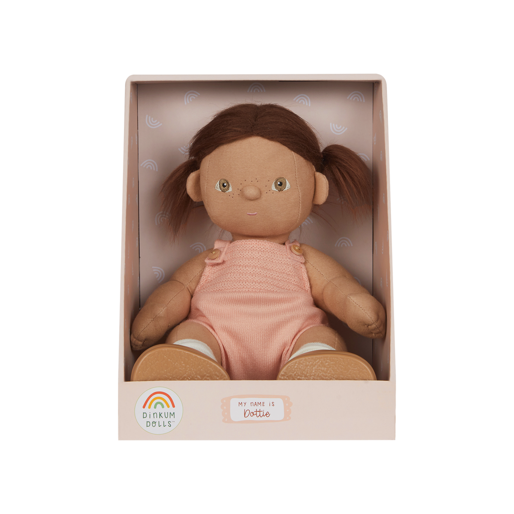 Doll in a pink outfit with brown hair in pigtails, sitting in a box with a visible brand logo.