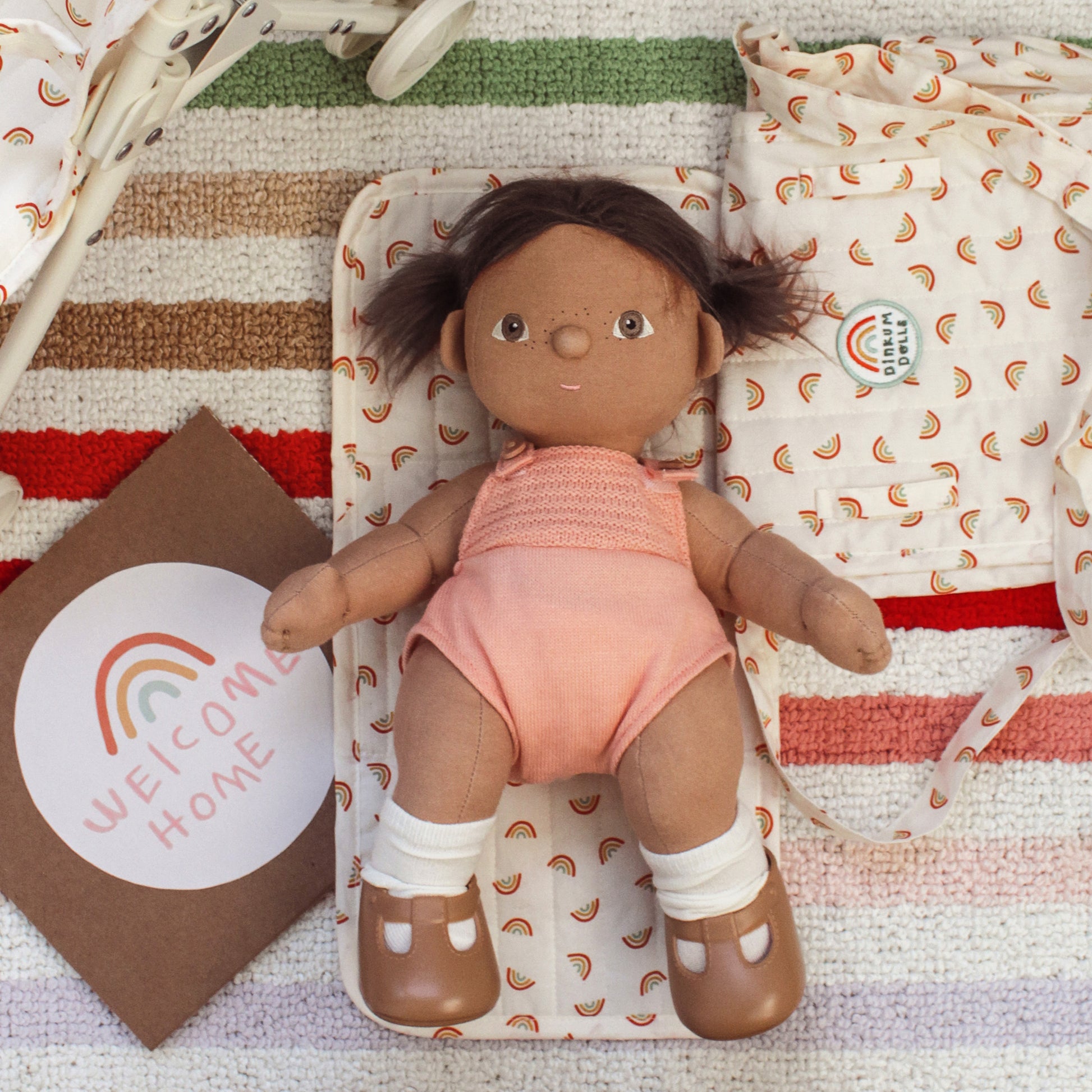 Doll in a pink outfit on a patterned blanket with 'Welcome Home' card