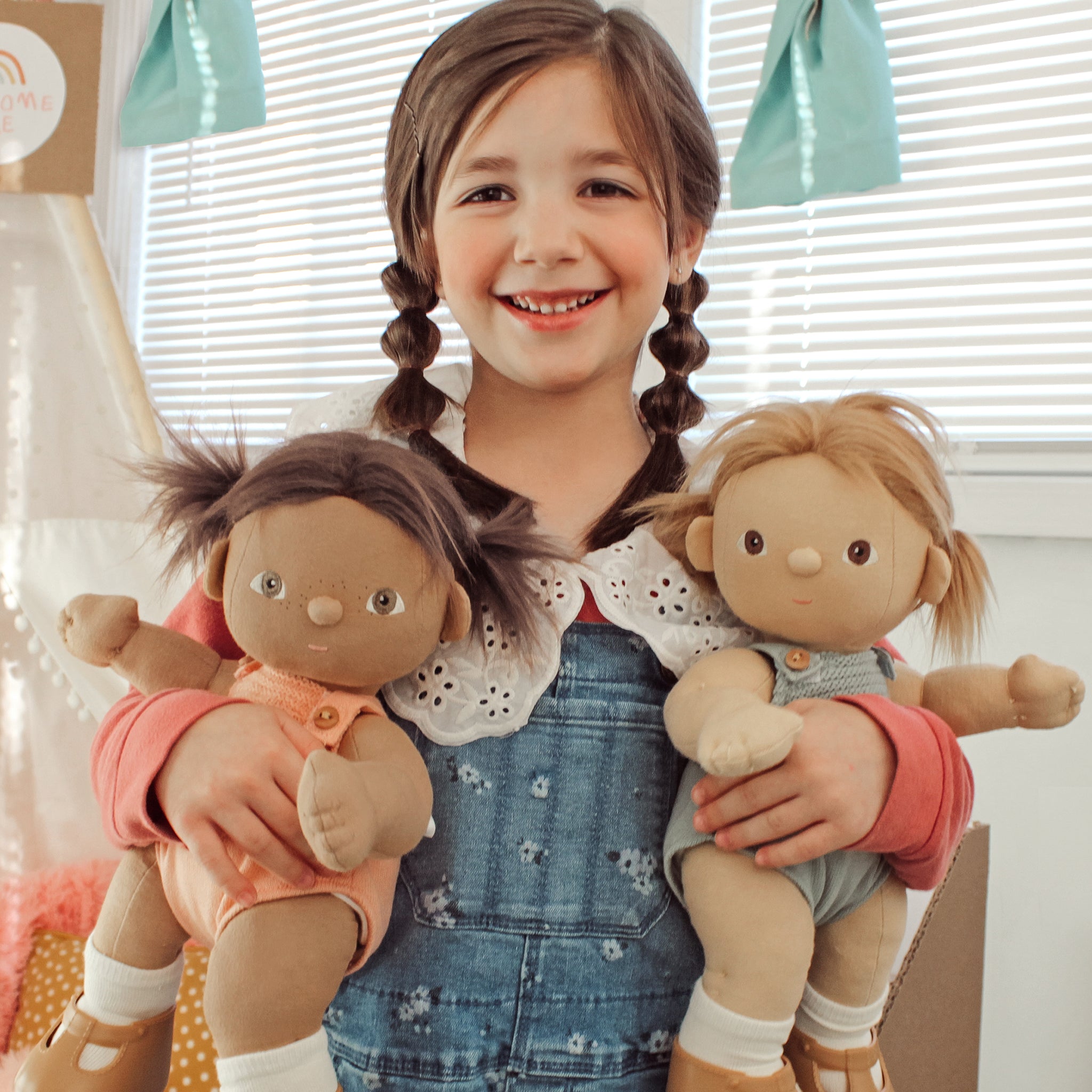 Young girl holding two dolls with a neutral background