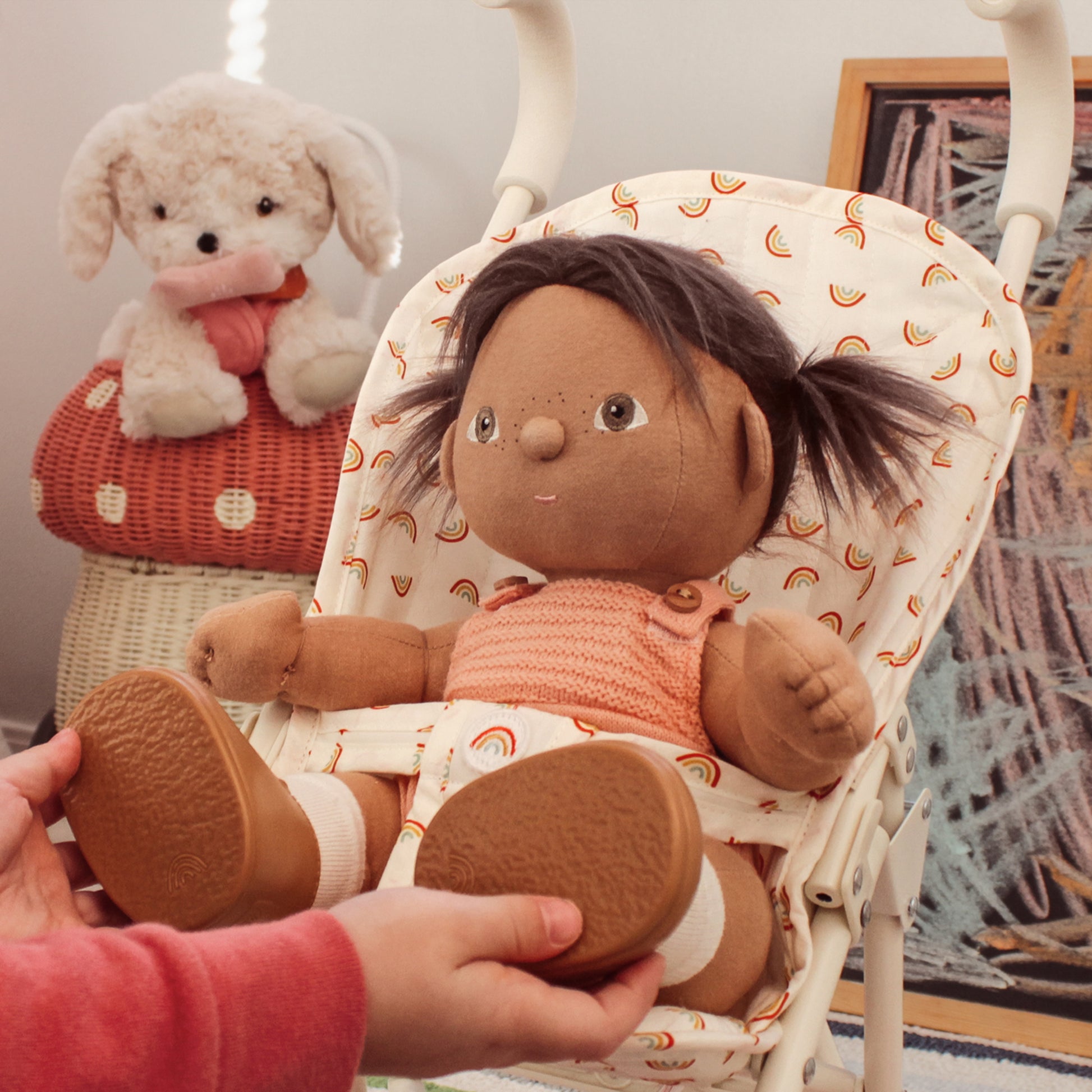 Stuffed doll with dark hair and brown shoes held by a hand, sitting in a patterned chair.