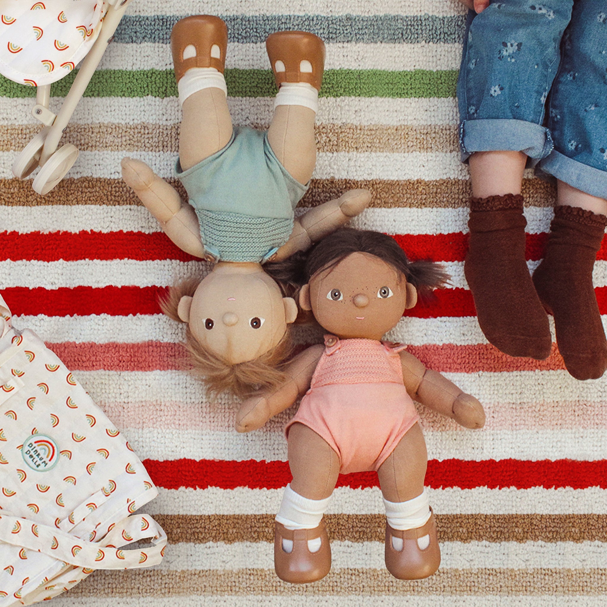 Two dolls lying on a striped rug with a child's legs visible.