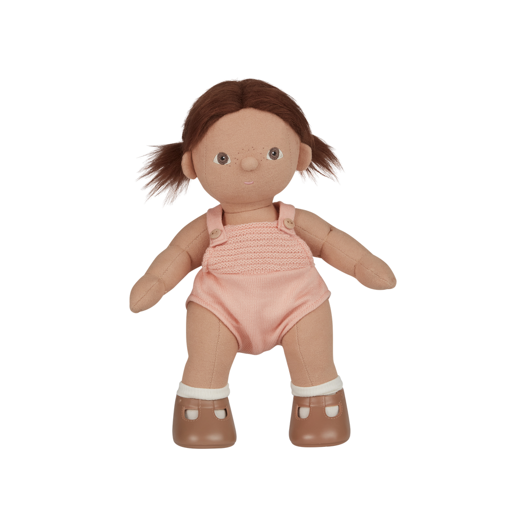 Toy doll with brown hair, pink romper, and white shoes on a white background