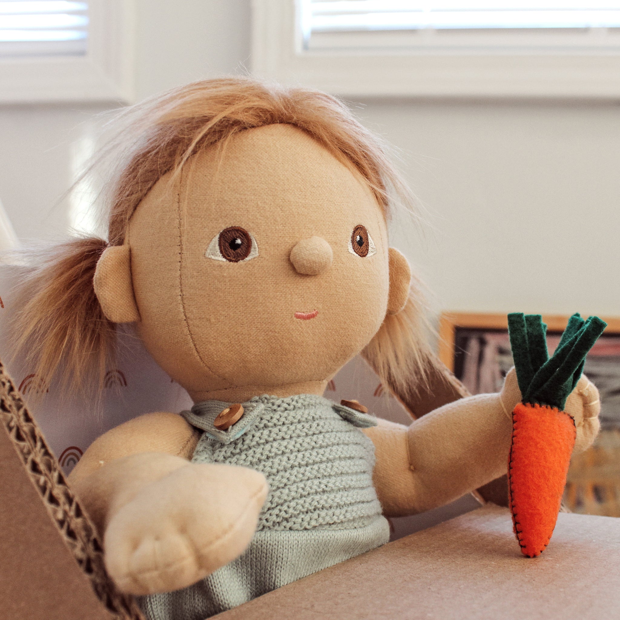 Textile doll with blonde hair and a green dress holding a felt carrot.
