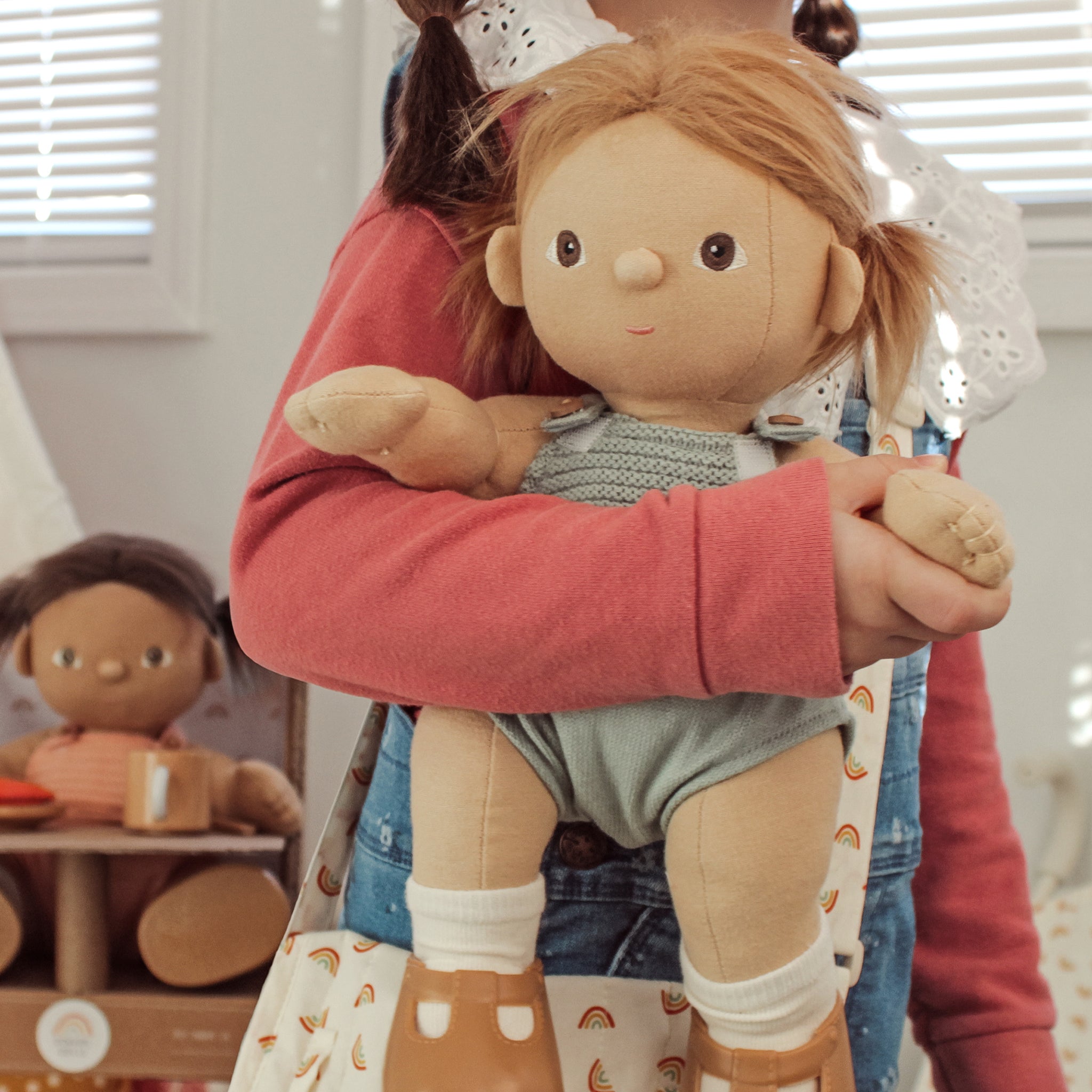 Person holding a doll with a neutral expression in a room with other dolls in the background