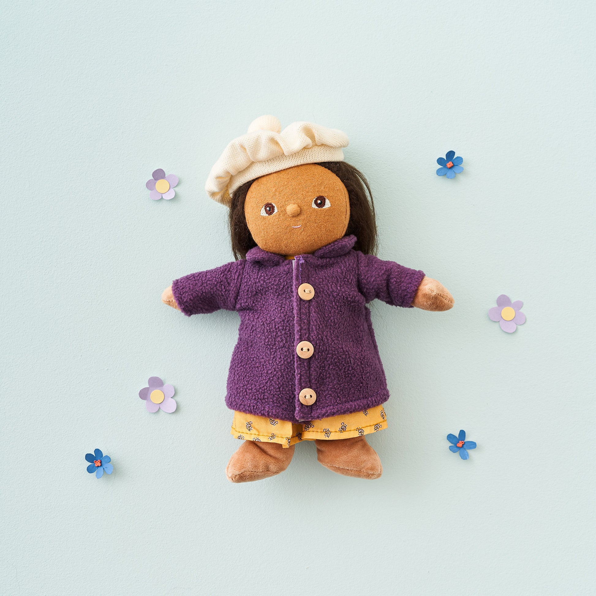 Toy figure wearing a purple coat and white hat on a light blue background with decorative flowers.