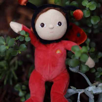 Plush toy dressed as a ladybug sitting among green plants