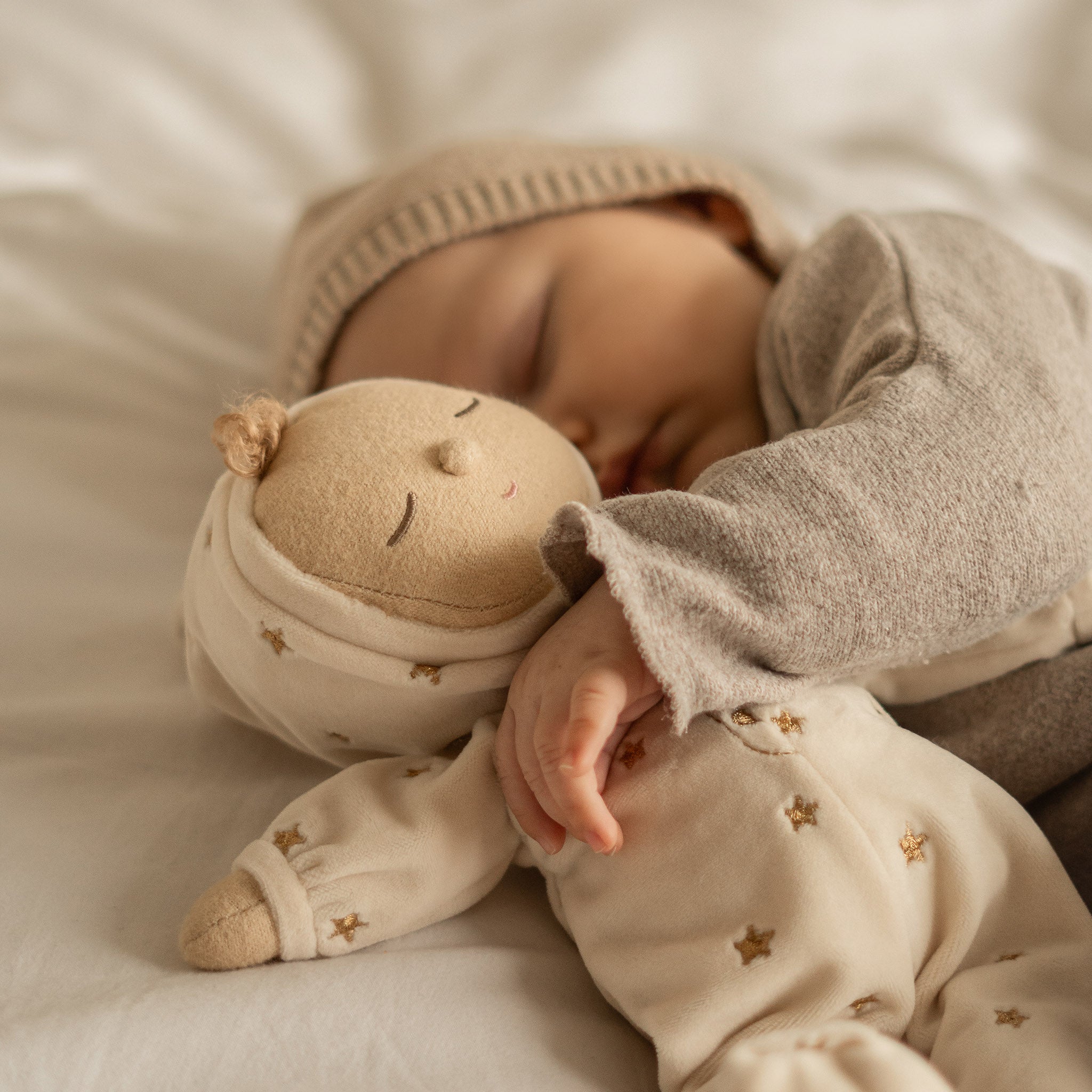 Baby in beige outfit holding a soft toy with star patterns on a soft surface