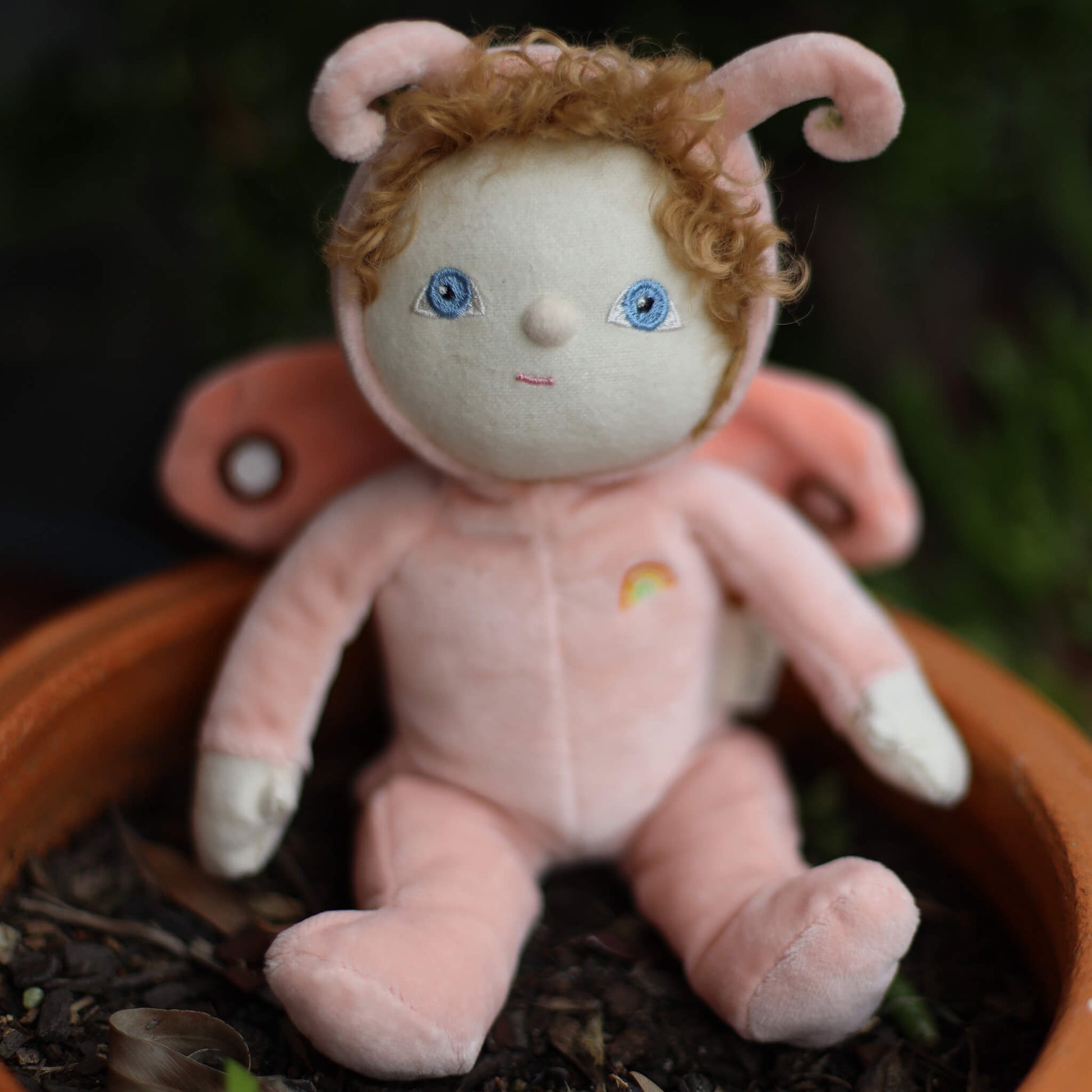 Pink moth doll with blue eyes and rainbow on a dark background