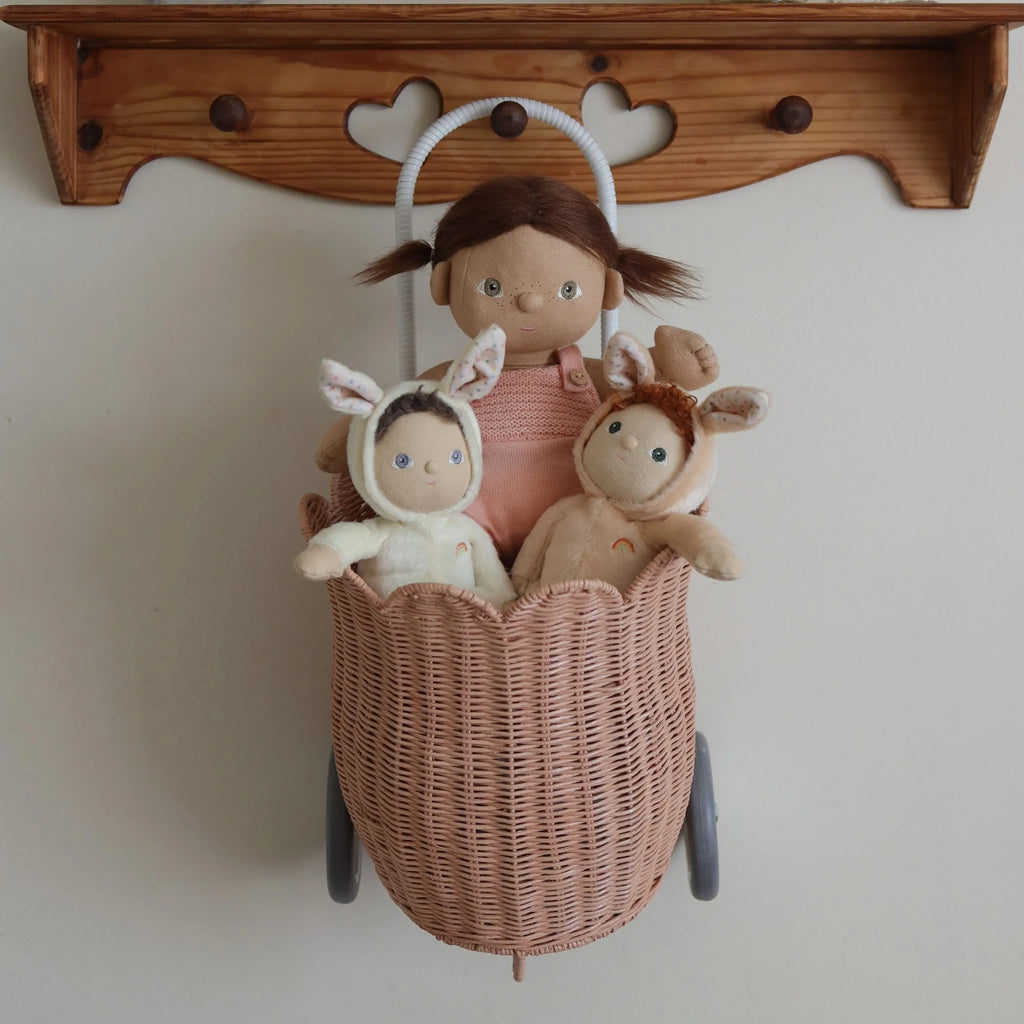 Wicker basket with a doll and two small stuffed animals against a wooden shelf.
