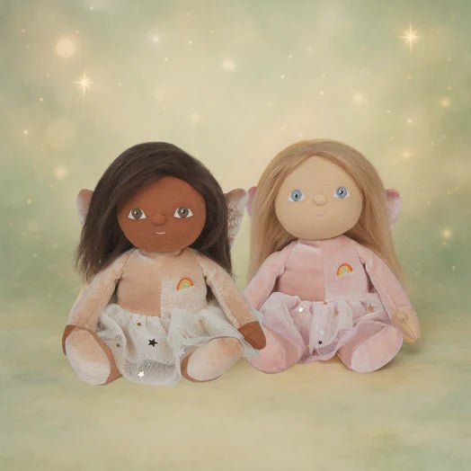 Two dolls with different skin tones sitting side by side on a soft, blurred background.