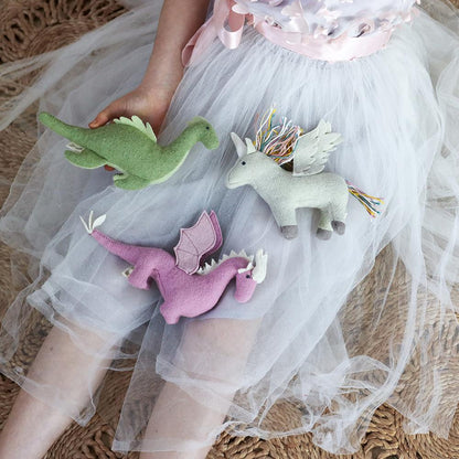 Children's toys including a green dinosaur, pink dragon, and gray unicorn held by a child in a tulle skirt.