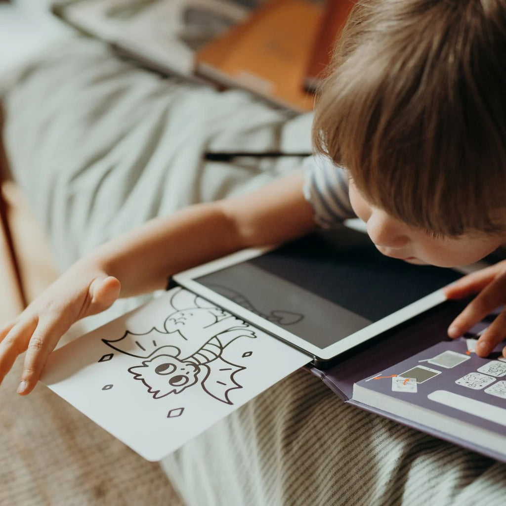 Child interacting with a tablet and coloring book on a bed