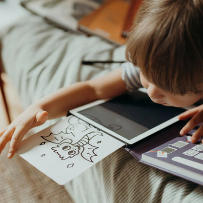 Child interacting with a tablet and coloring book on a bed