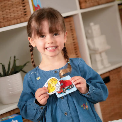 Young girl holding two colorful cards with a red car and yellow sponge design, smiling in a home setting.