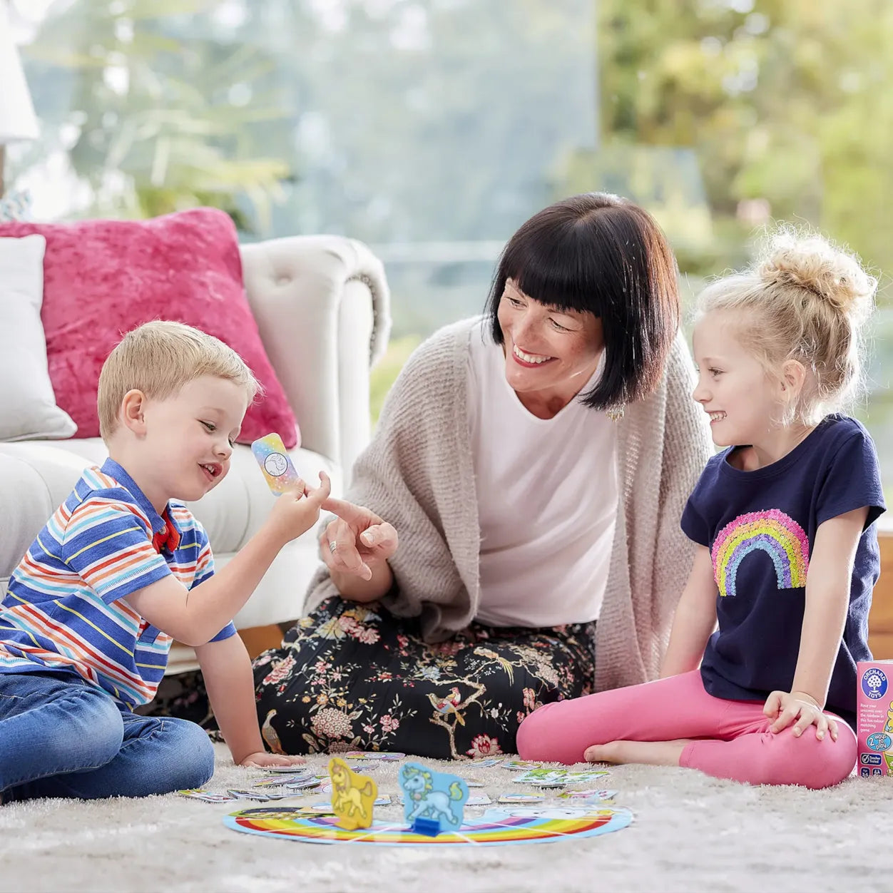 Woman and two children playing with toys on a carpeted floor.